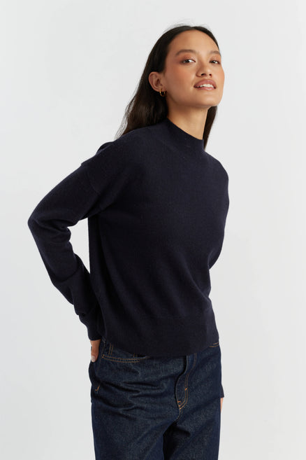 Woman wearing a navy sweater and jeans on a white background