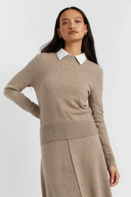 Woman wearing a beige sweater with a white collar against a light gray background