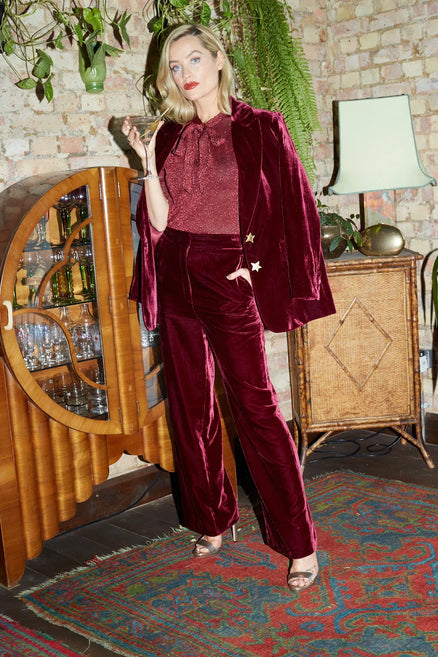 Woman in burgundy velvet outfit standing in a room with decorative elements.