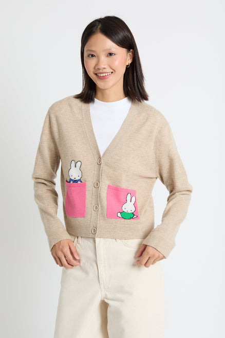 Woman wearing a beige cardigan with cartoon character pockets on a white background