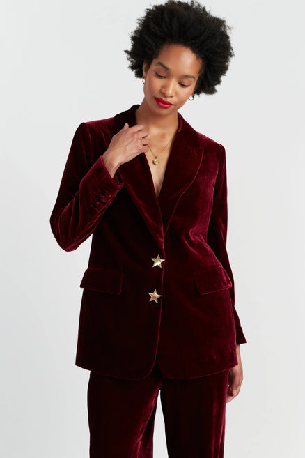 Woman wearing a burgundy velvet suit with star buttons on a light gray background