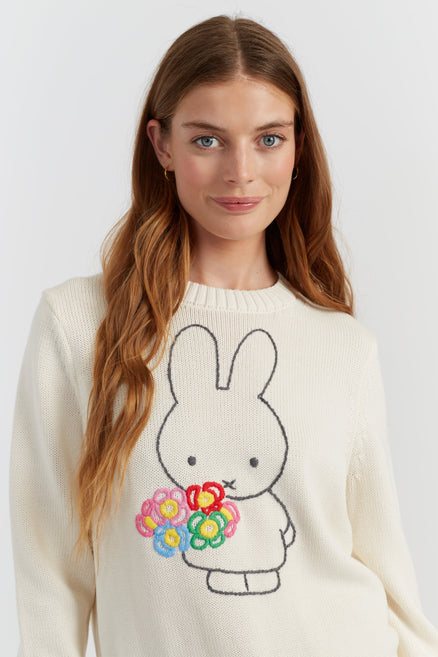 Woman wearing a cream sweater with a bunny design holding flowers on a white background