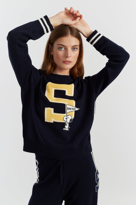 Person wearing a navy sweater with a large yellow letter 'S' and a small graphic on a white background